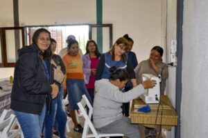 A group of women are watching another woman teach them how to use a sewing machine.